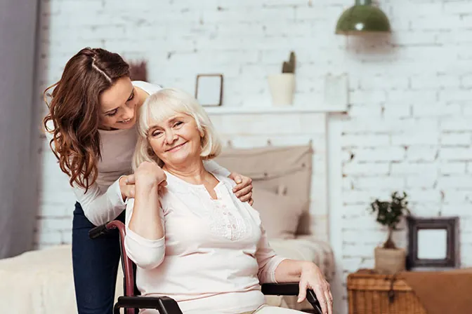Carer hugging a smiling elderly woman in a wheelchair at home